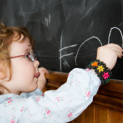 child writing name on blackboard
